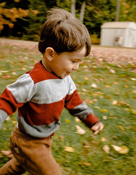 Child running joyfully in a garden, surrounded by autumn leaves, illustrating the importance of visual processing skills for learning and development.